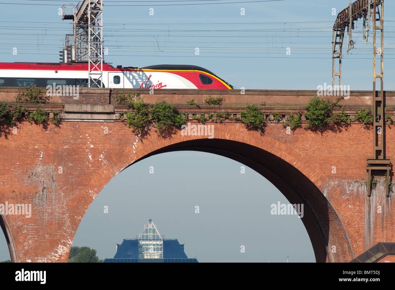 A Virgin train travels across Stockport Viaduct,built with 11 million bricks. Co-op Bank Pyramid building in the background. Stock Photo