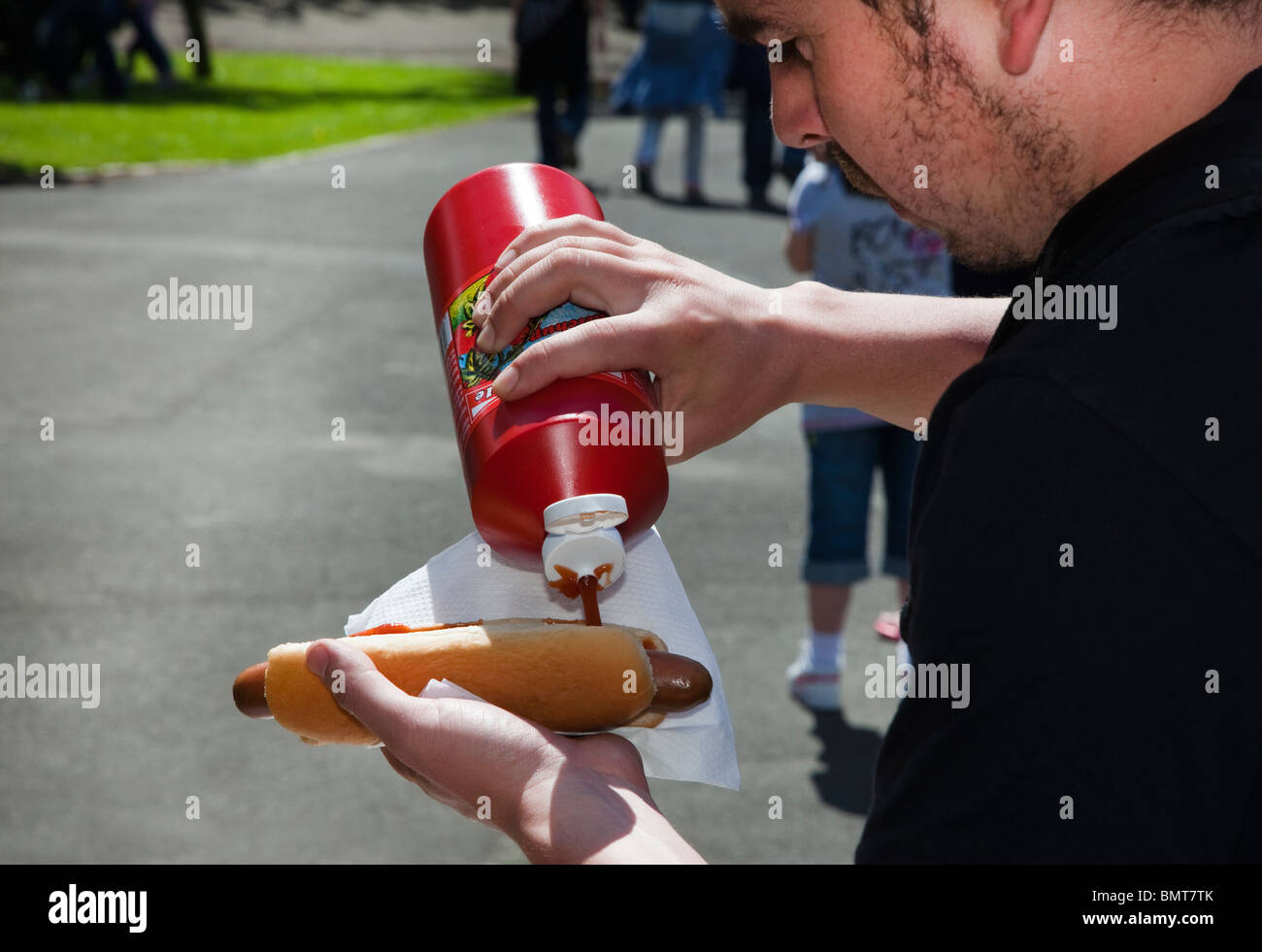 Man putting tomato sauce onto a roll and sausage, West End Festival, Glasgow, Scotland, UK, Great Britain Stock Photo