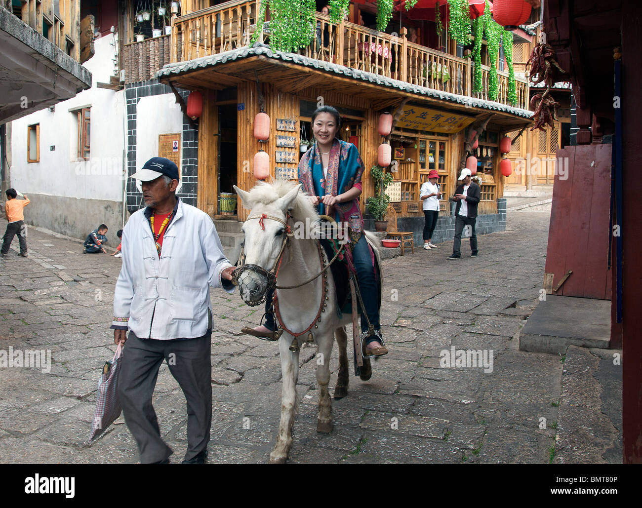 Woman on horse being lead through street Lijiang Old Town Yunnan China Stock Photo