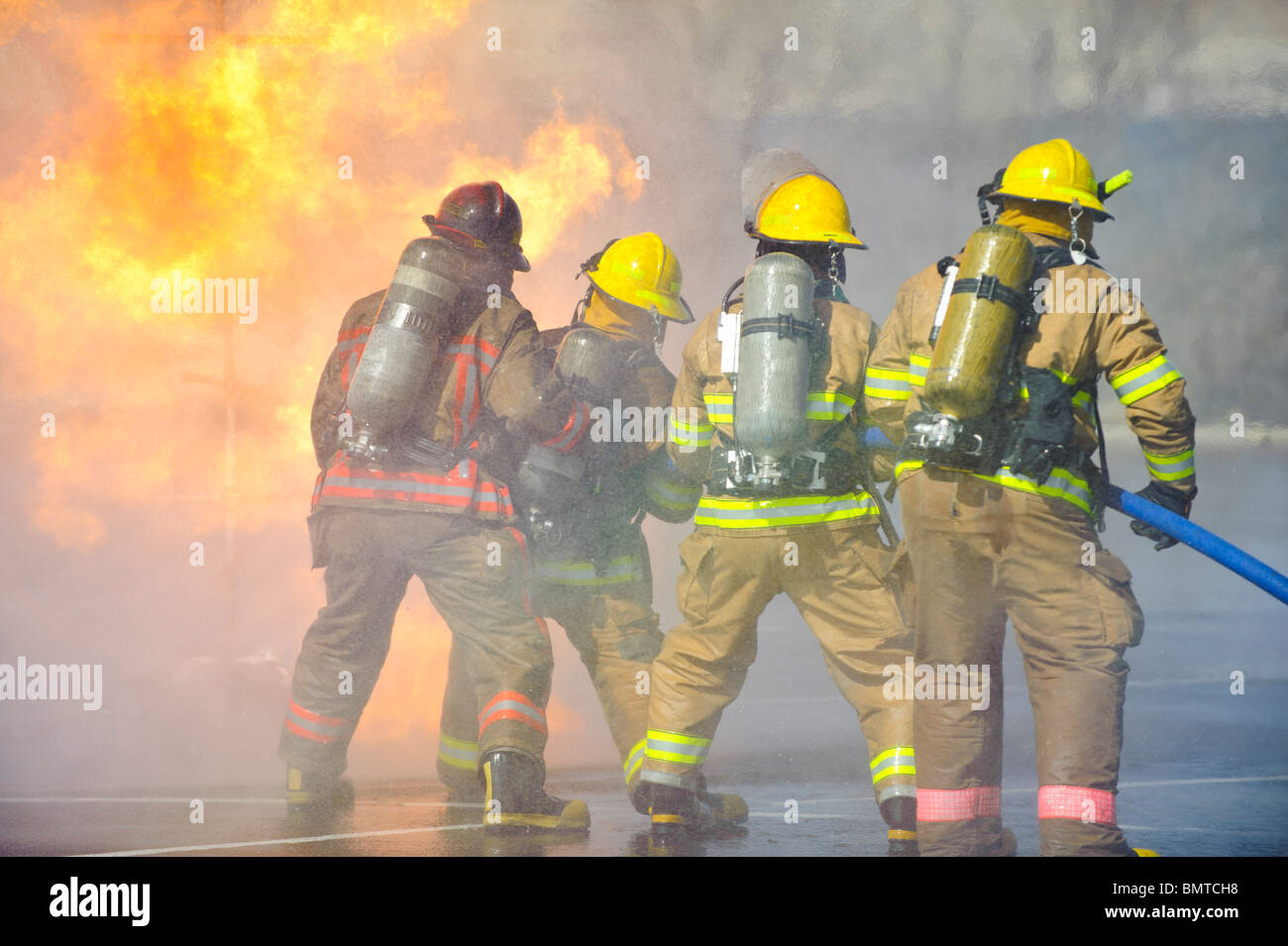 Directed by an officer in a red helmet, firefighters attack a propane fire during a training exercise. Stock Photo