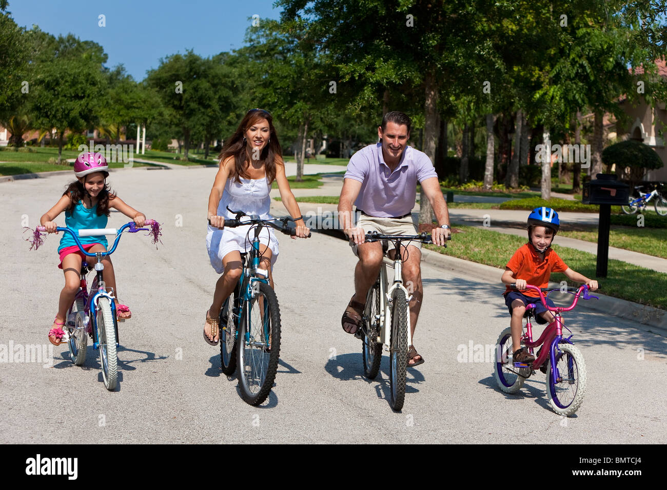 A modern family of two parents and two children, a boy and a girl, cycling together. Stock Photo