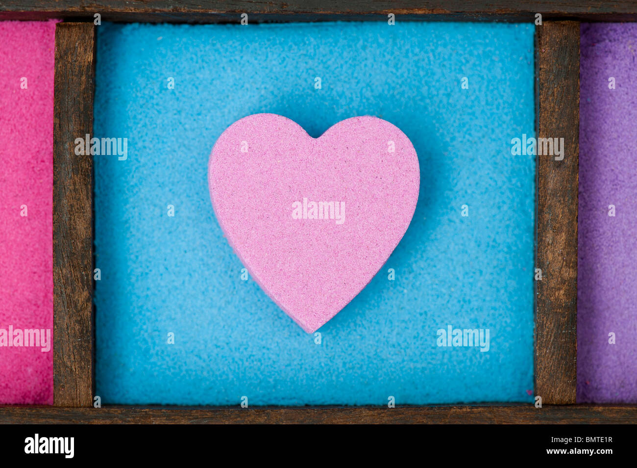 Pink heart shape on blue sand in a wooden tray Stock Photo
