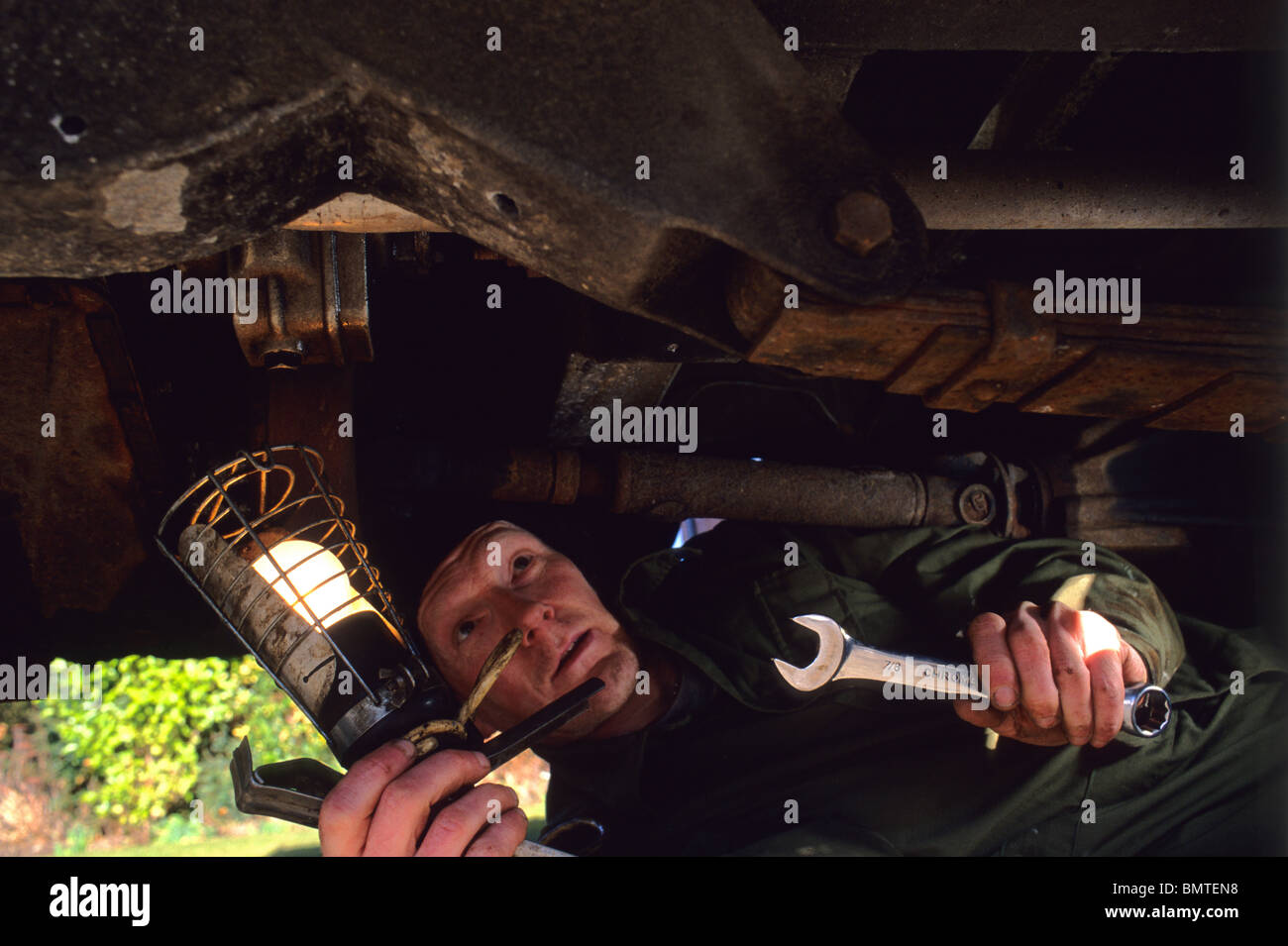 mechanic working underneath vehicle using spanner and inspection lamp Stock Photo