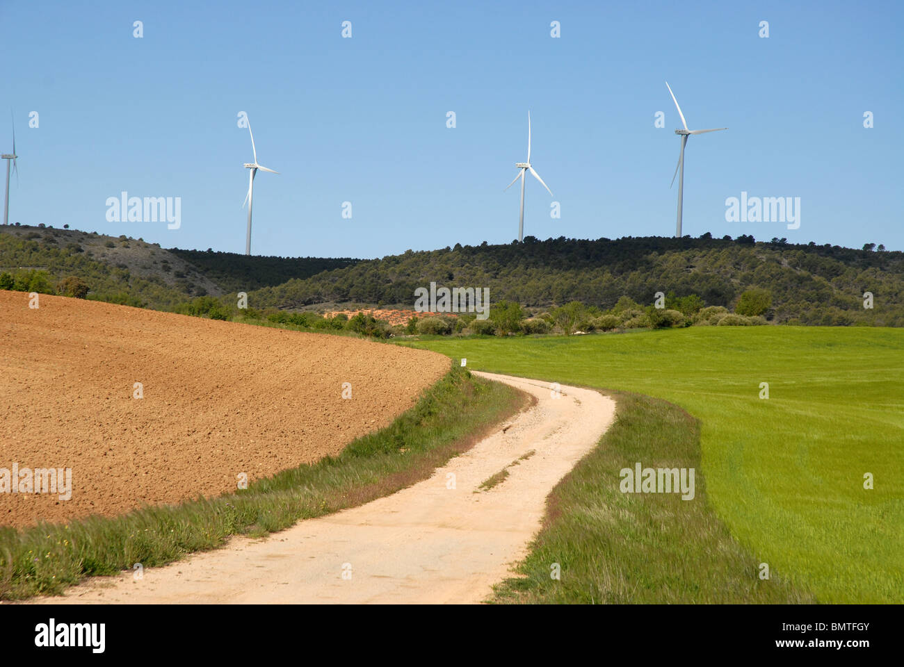 rural road through wheat fields to aerogenerators on the horizon, near Huete, Cuenca Province, Castile-La Mancha, Spain Stock Photo