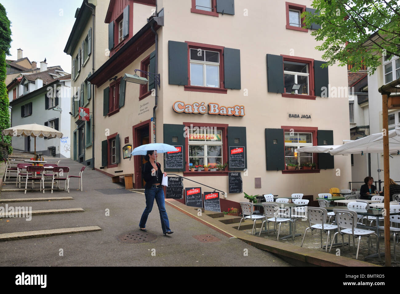 Woman with an umbrella passing by a cafe in light rain in the old city of Basel Stock Photo