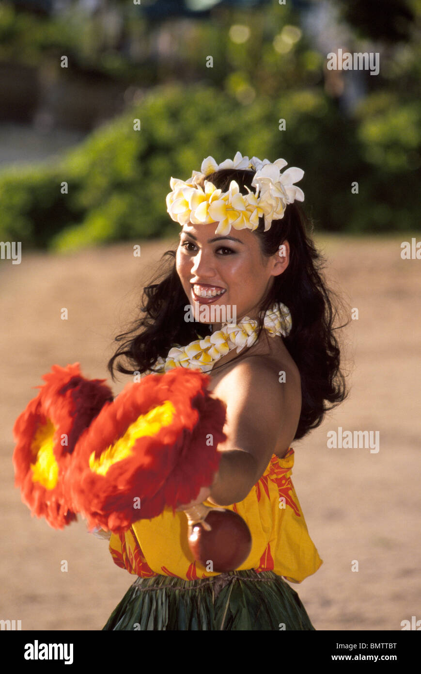 A Hawaiian hula dancer performs with feather gourd rattles ('uli'uli) on   Waikiki Beach during a luau for tourists in Honolulu, Oahu, Hawaii, USA. Stock Photo