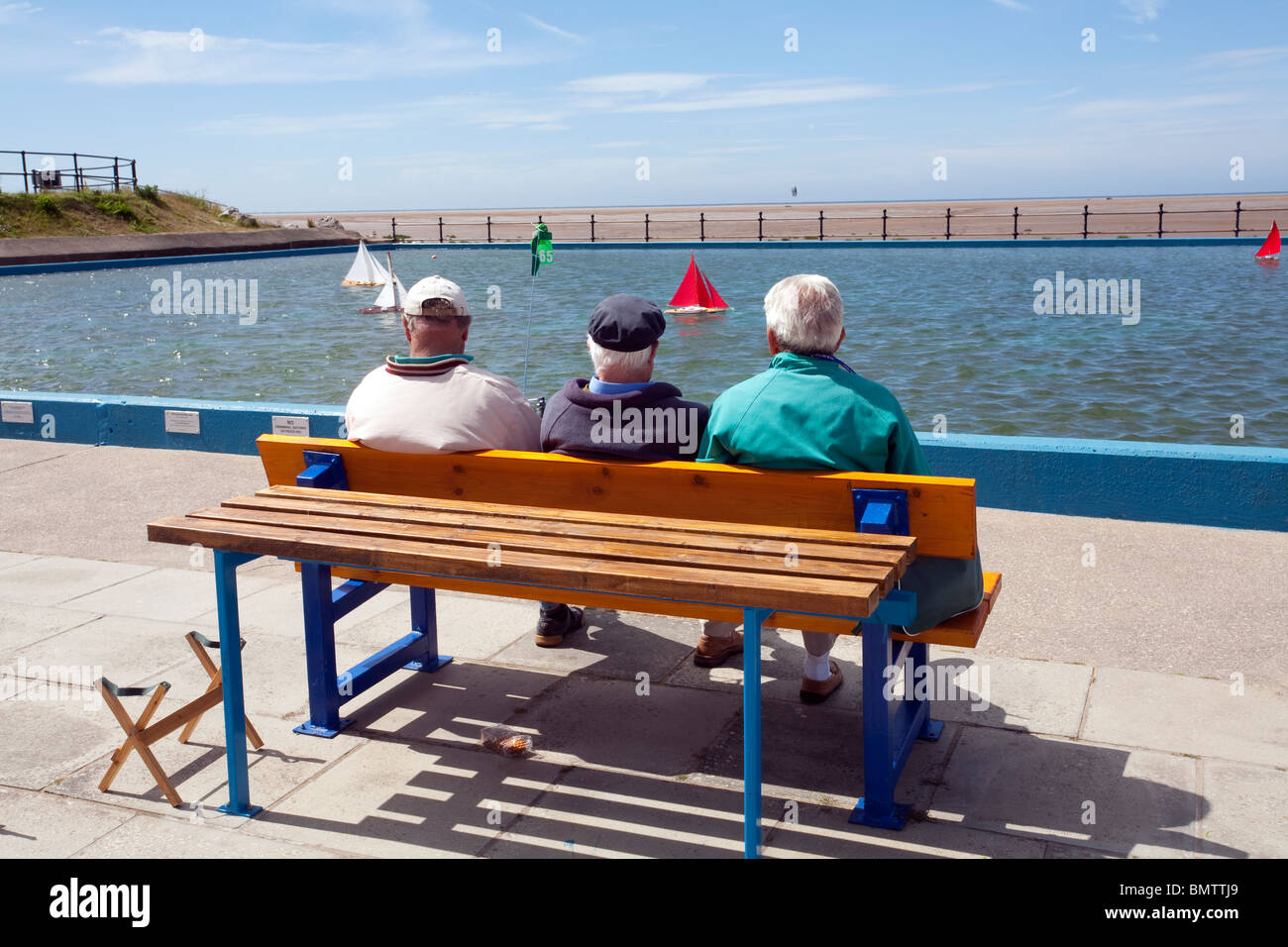Hoylake model boating lake in the sunshine. Three gentlemen enjoying the weather and the thrill of a popular pastime in the sun. Stock Photo