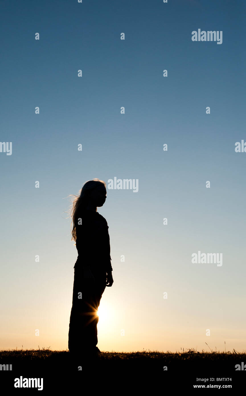 Solitary Young Girl standing against a sunset. Silhouette Stock Photo ...