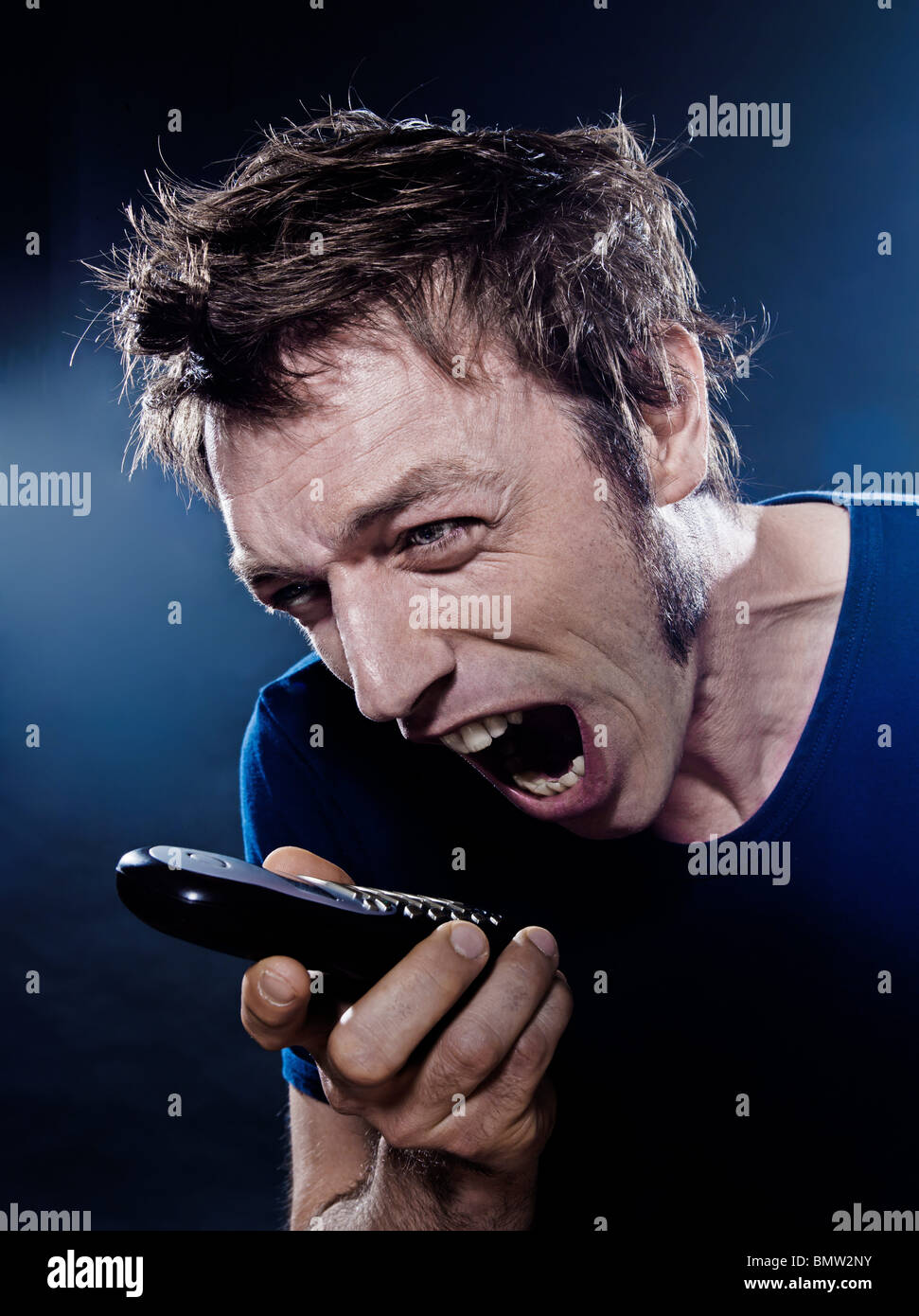 studio portrait on black background of a funny expressive caucasian man yelling at phone Stock Photo