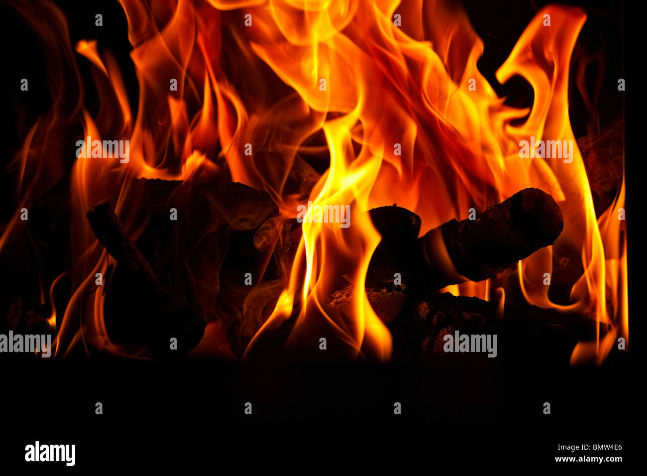 Burning logs silhouetted against flames in a hearth. Stock Photo