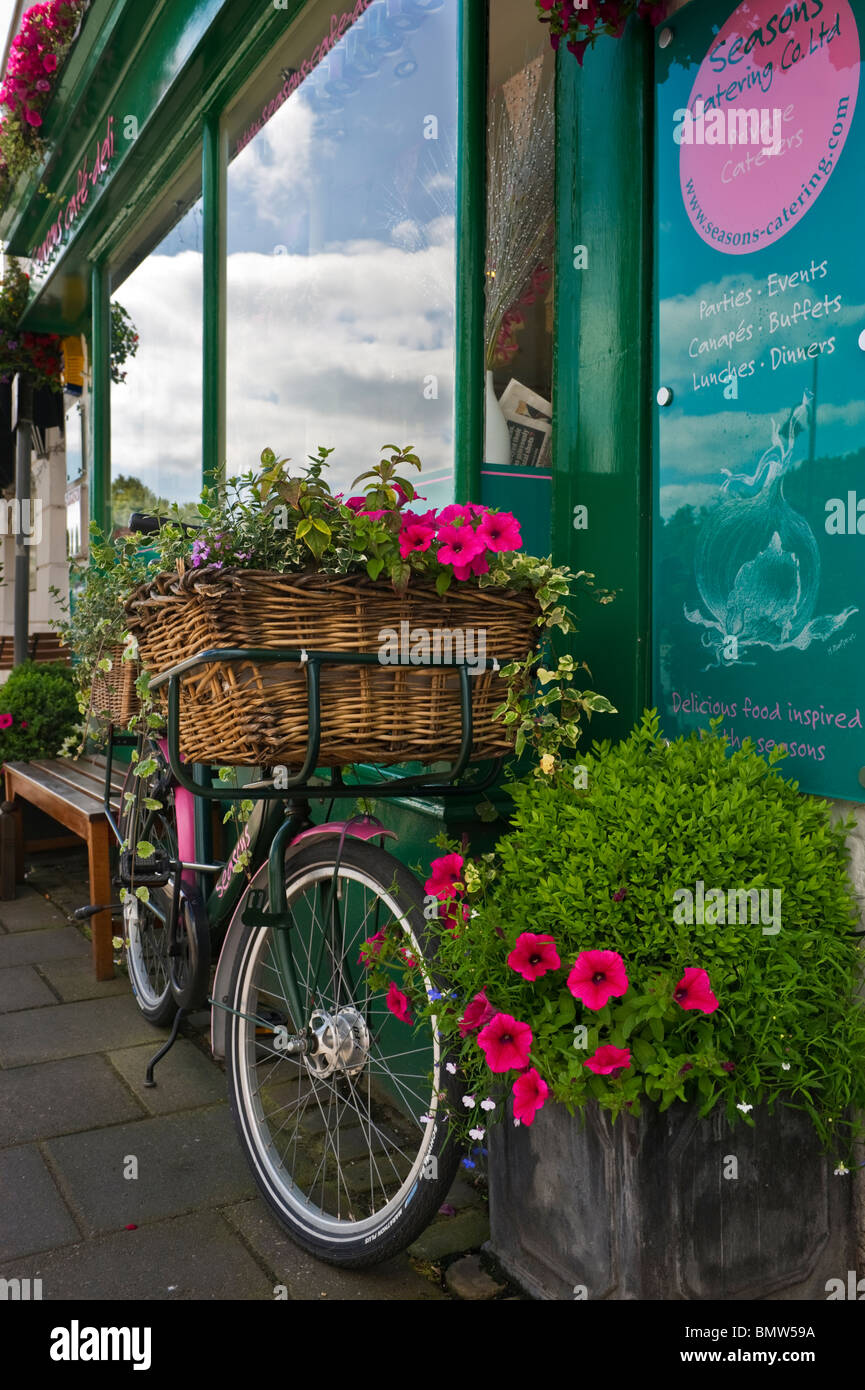 A delivery bicycle with front basket full of marigolds and flowers outside a cafe window in old Amersham Buckinghamshire UK Stock Photo