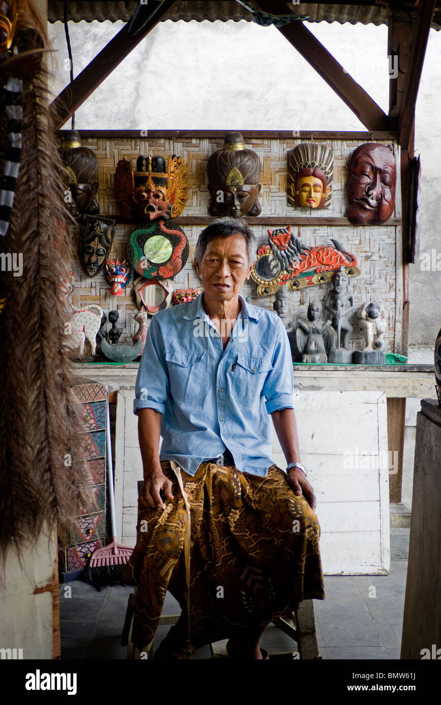 A Balinese mask maker waits for customers at the Ubud, Bali Public Market. The masks are Hindu themed figures in mythology. Stock Photo
