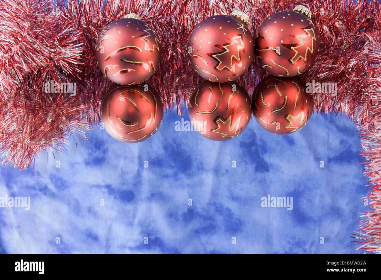 three red Christmas baubles with tree outlines, red and white tinsel, reflections and copyspace Stock Photo