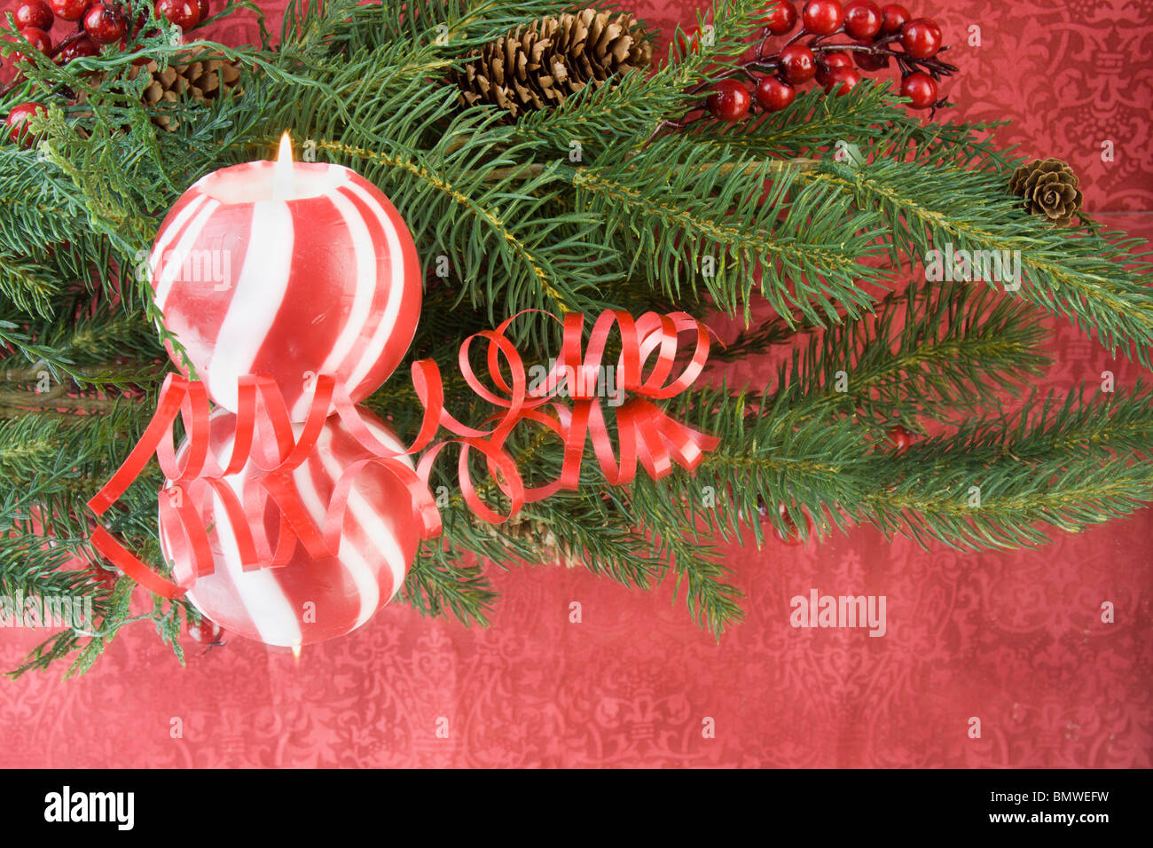 red striped Christmas candle with fir branch, curly ribbon, reflections and copyspace Stock Photo