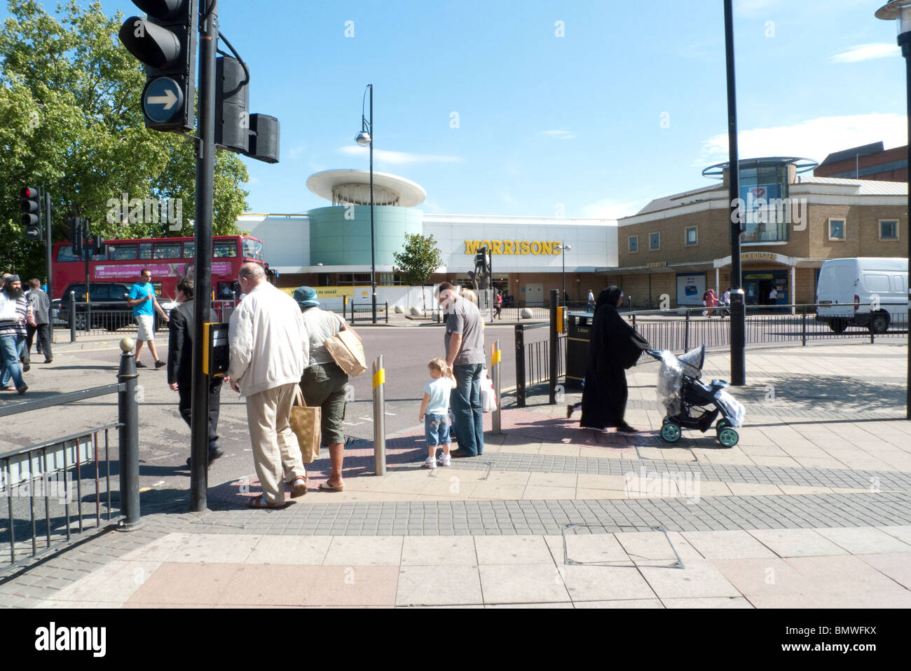 Pedestrians crossing street at traffic lights and Muslim woman with pram near Morrisons supermarket in Stratford East London England UK  KATHY DEWITT Stock Photo