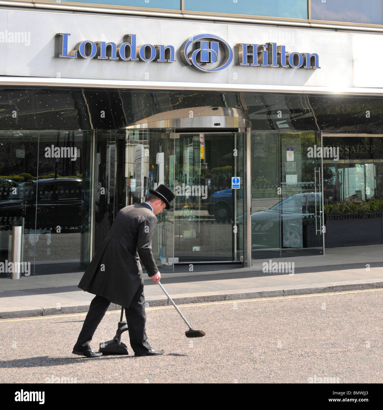 London West End Mayfair Park Lane Hilton Hotel sign close up main front entrance & canopy doorman in uniform sweeping approach road clean England UK Stock Photo