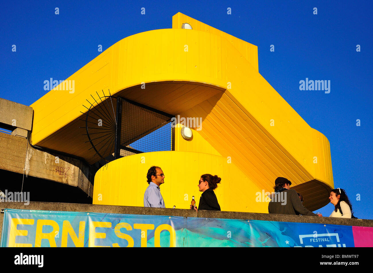 People Socializing drinking on balcony with abstract yellow stairs Stock Photo