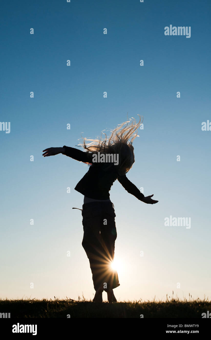 Young Girl energetically having fun and dancing around at sunset. Silhouette Stock Photo