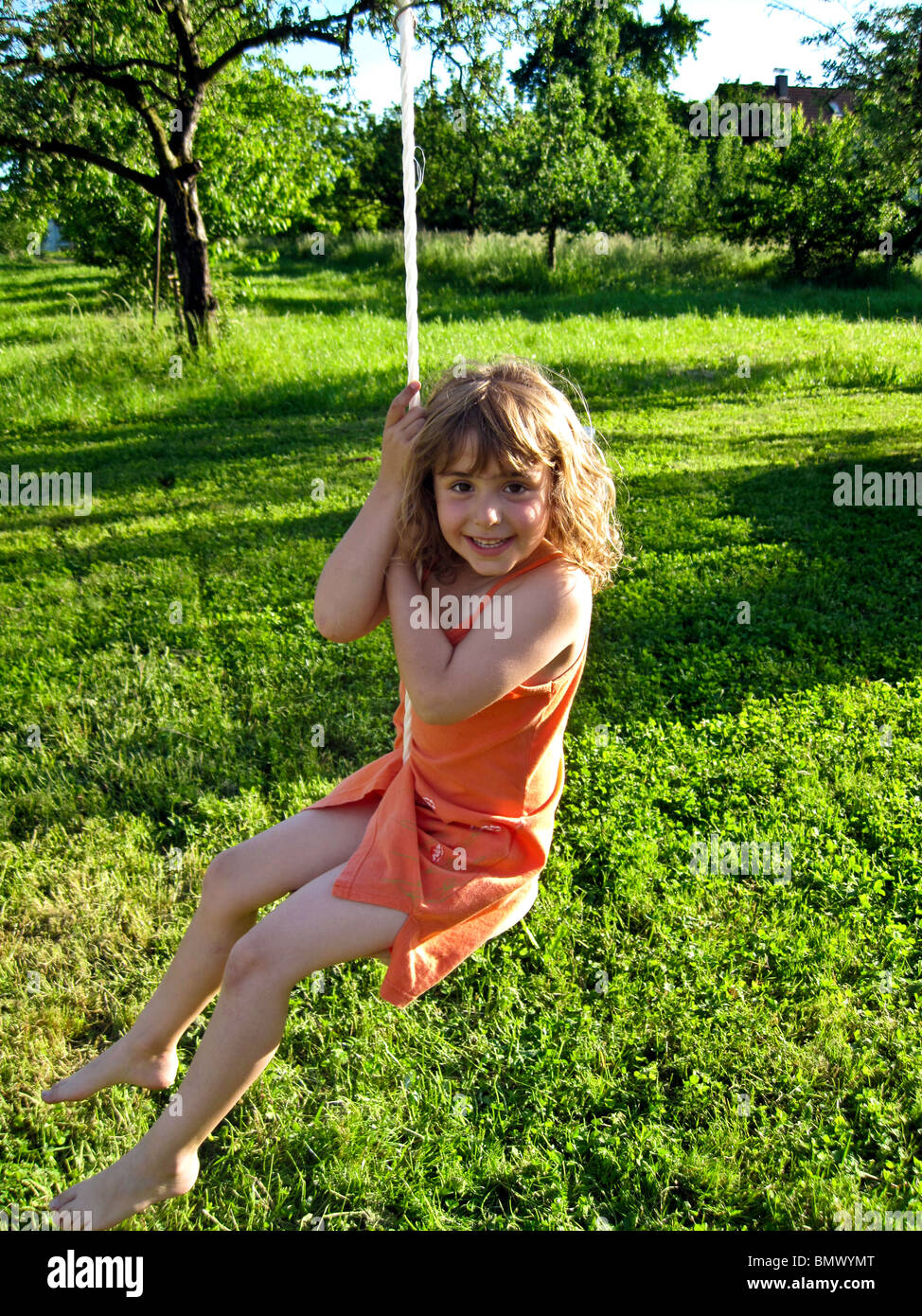 german preteen  German Girl in orange dress playing on an outdoor swing with a  green pasture behind her.. Model released Stock Photo - Alamy