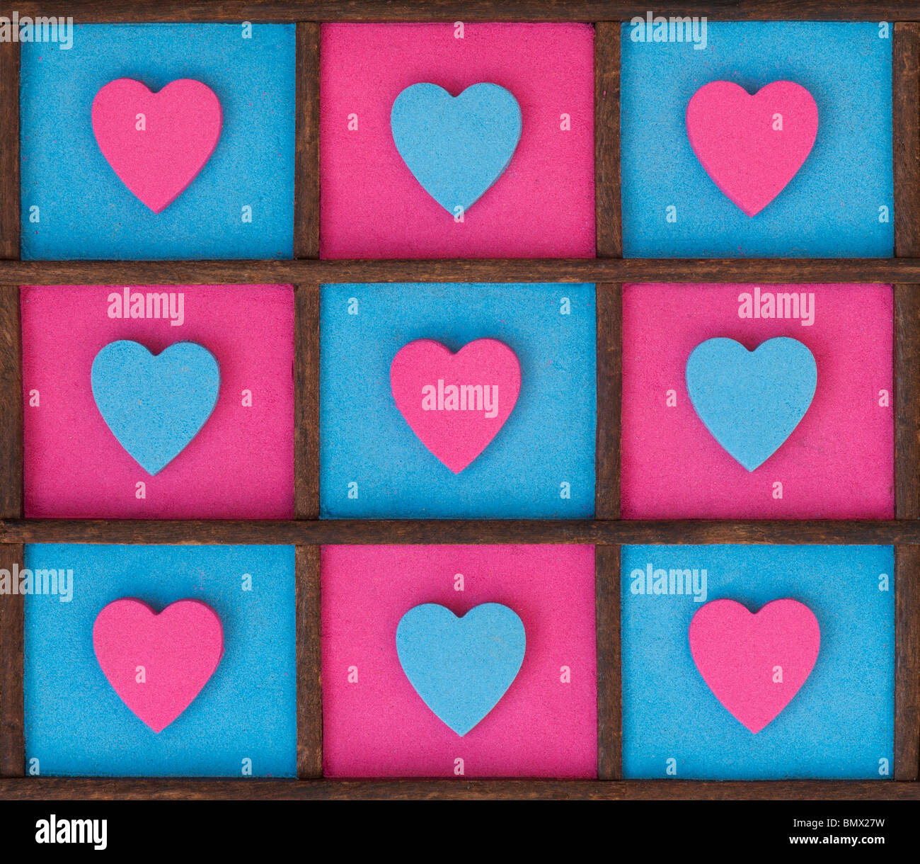 Multicoloured heart shape patterns in a wooden tray. Pink and blue Stock Photo