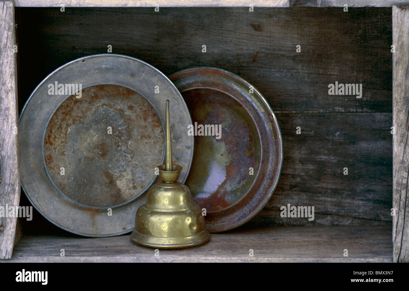 Spare parts for your old car. Rusted hubcaps and dented oil can on weathered wooden shelf. Stock Photo