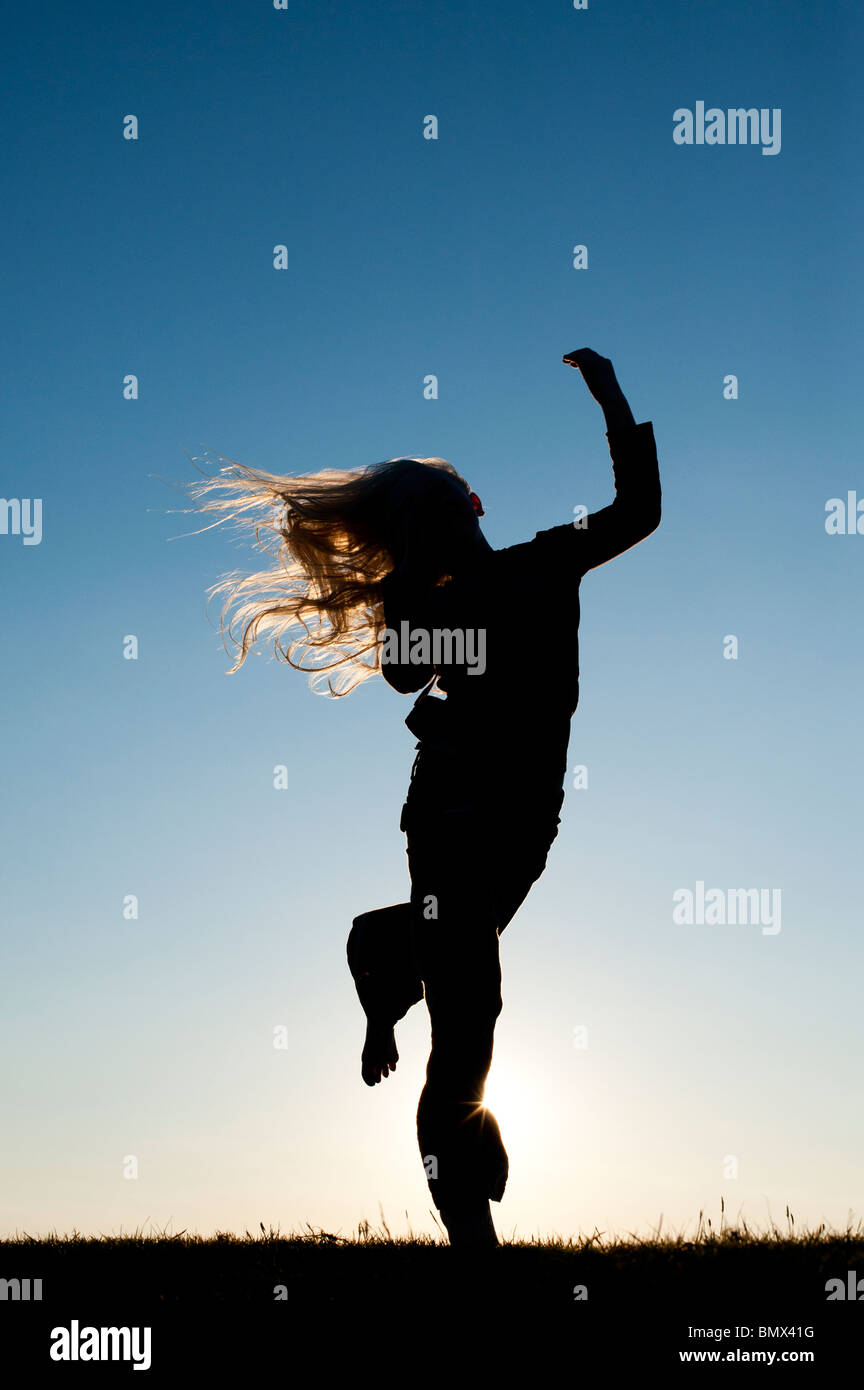 Young Girl energetically having fun and dancing around at sunset. Silhouette Stock Photo