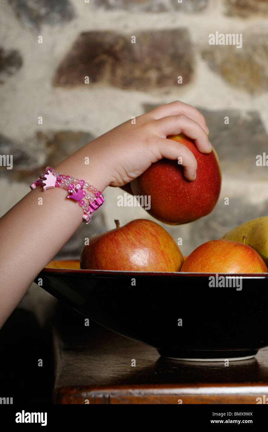 Stock photo of a little girls hand reaching up to take an apple out of the fruit bowl. Stock Photo