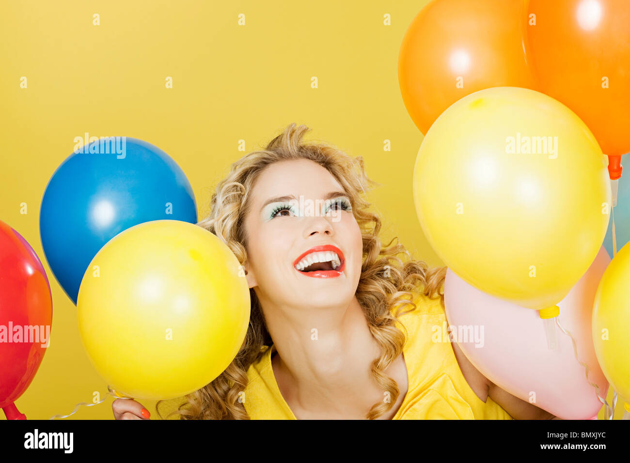 Young blonde woman with balloons against yellow background Stock Photo