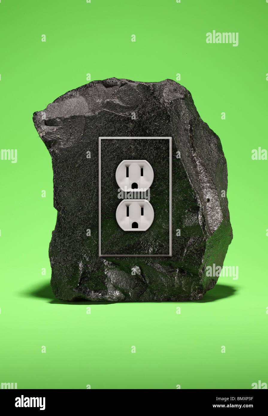 A large black chunk of coal with an electrical power outlet fixture on a bright green background. Stock Photo