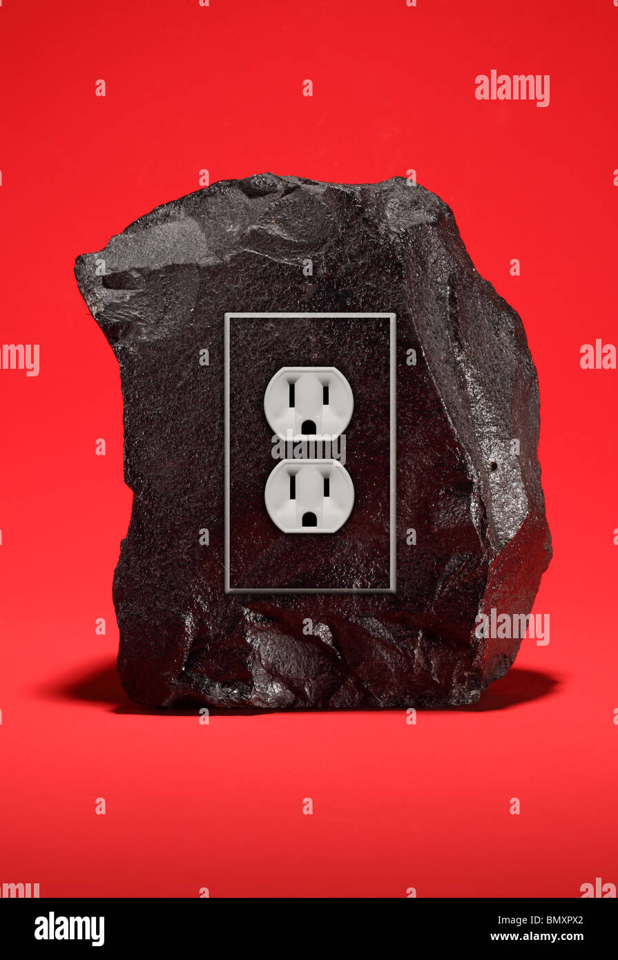 A large black chunk of coal with an electrical power outlet fixture on a bright blue background. Stock Photo