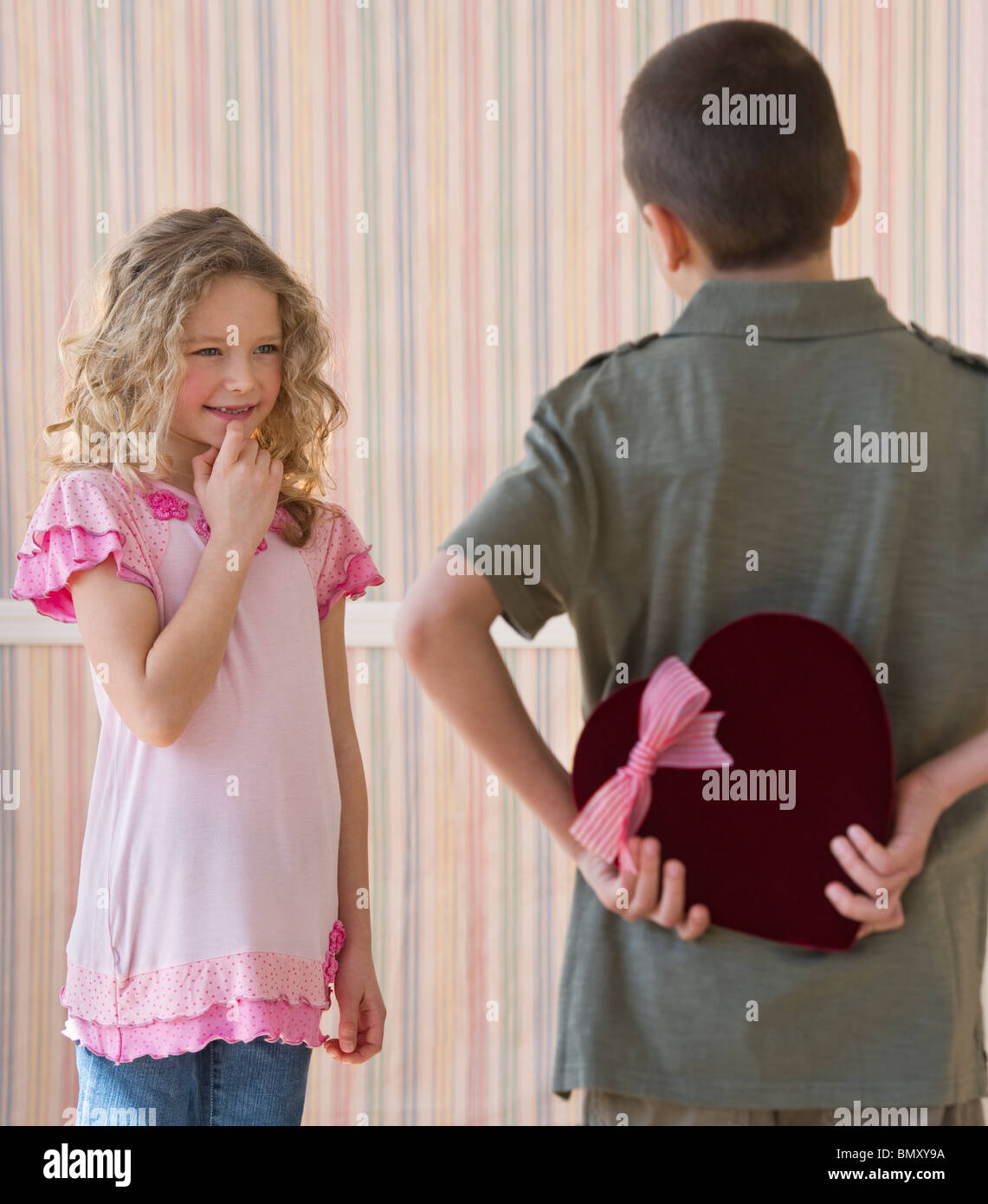 Young boy hiding a box of chocolates from young girl Stock Photo