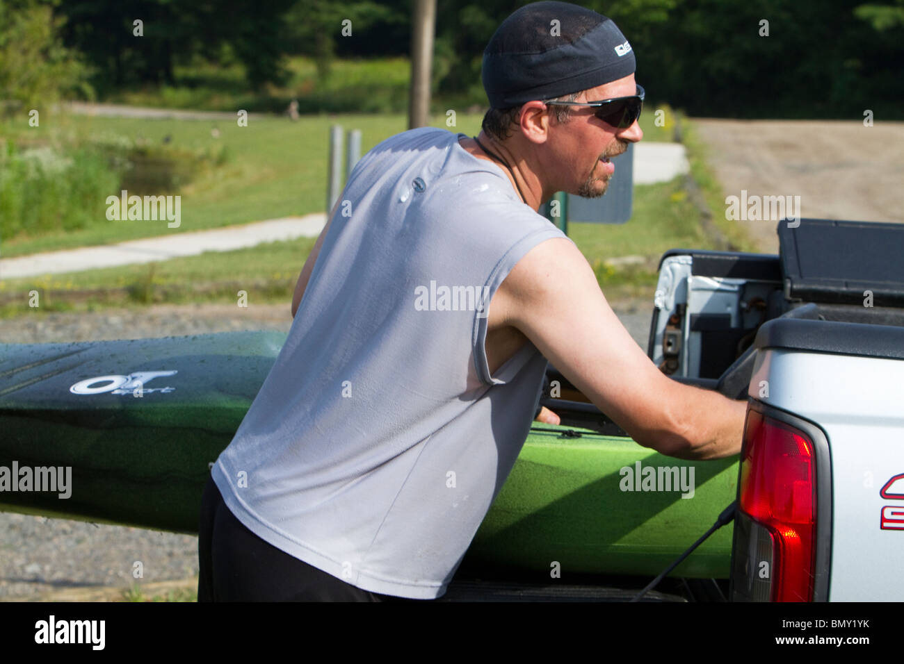 A man putting a kayak in the back of a pickup truck lorry Stock Photo