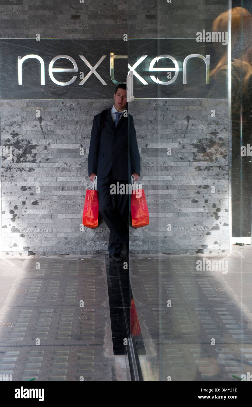 Man with red carrier bag in front of Next store on Oxford Street, London, UK Stock Photo