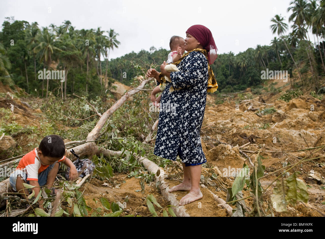 Jaryanis, 35, comforts her baby, Aisha, as rescue workers search the rubble of a landslide, triggered by the earthquake, Stock Photo