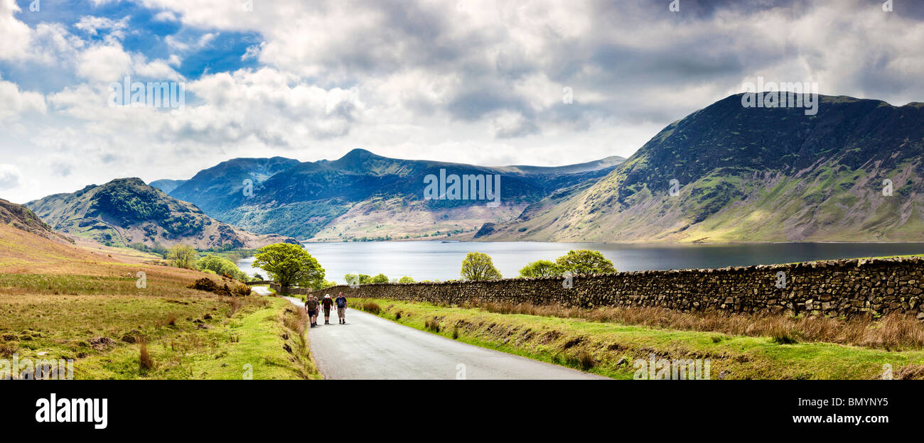 Walkers hiking on the road past Crummock Water, the Lake District, Cumbria, England, UK - panorama, pano Stock Photo
