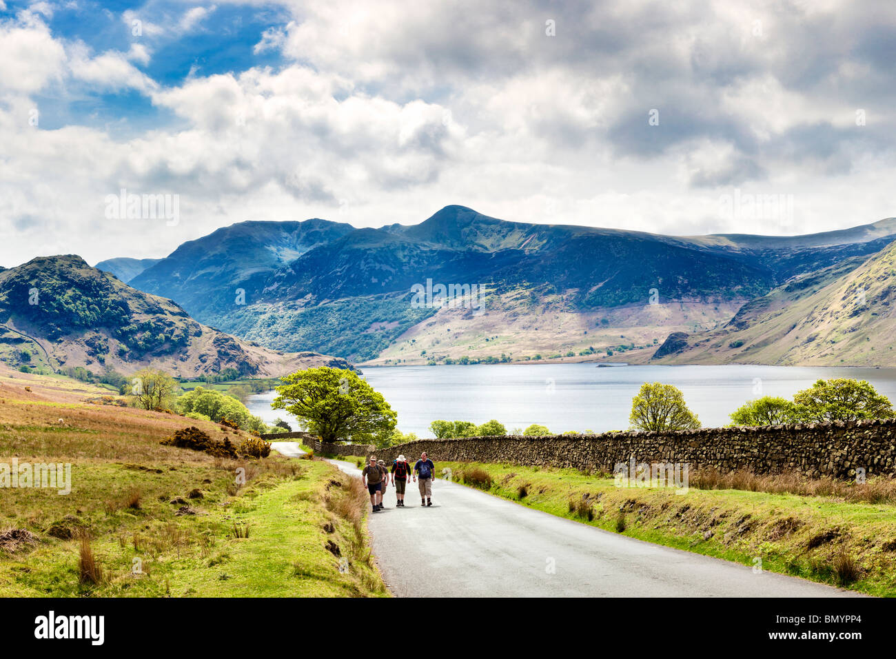 Walkers walking on the road past Crummock Water, Lake District, England, UK with High Stile and Red Pike mountains in spring Stock Photo