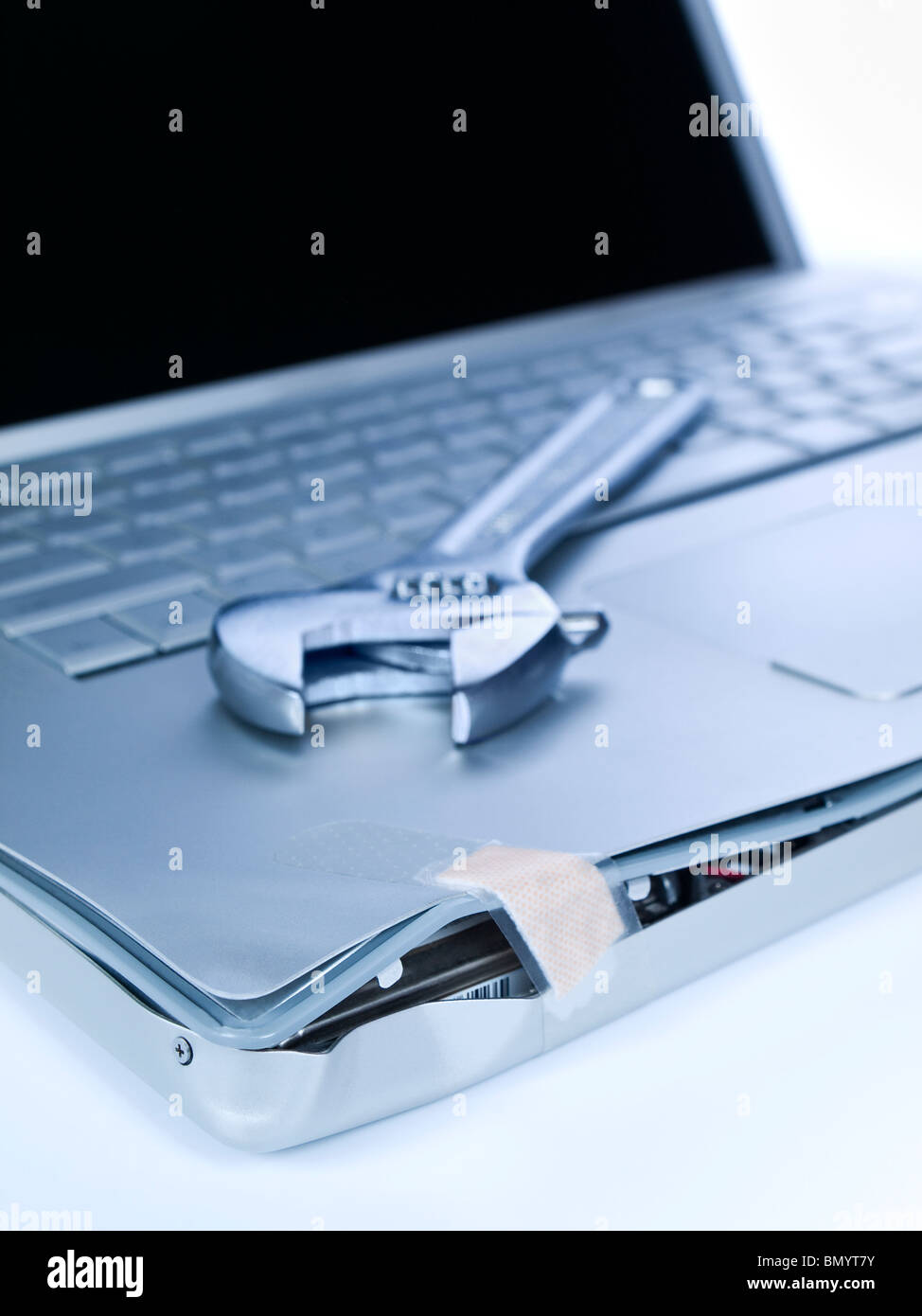 A band aid is fixing a damaged laptop. A spanner is over the computer. Stock Photo