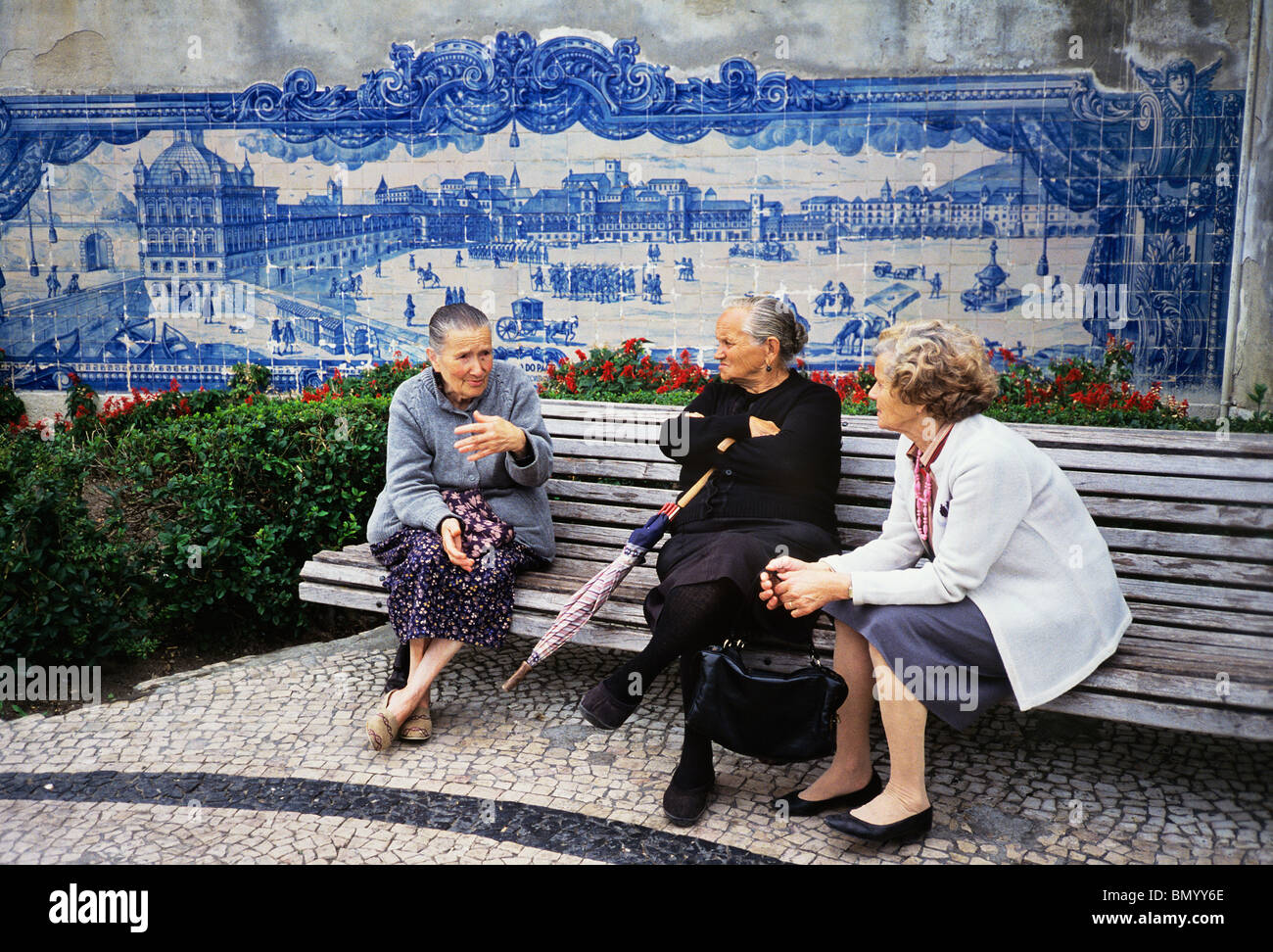 Women chat beside a tile panel in Lisbon's Alfama that shows the Palace Square as it was before the Great Earthquake o 1755 Stock Photo