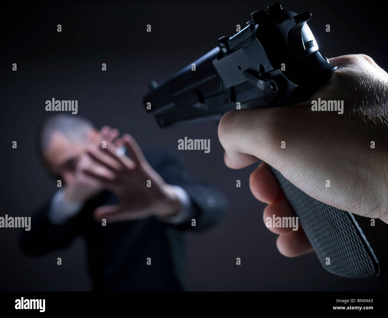 A threatening hand pointing a gun on an unarmed helpless businessman. Stock Photo