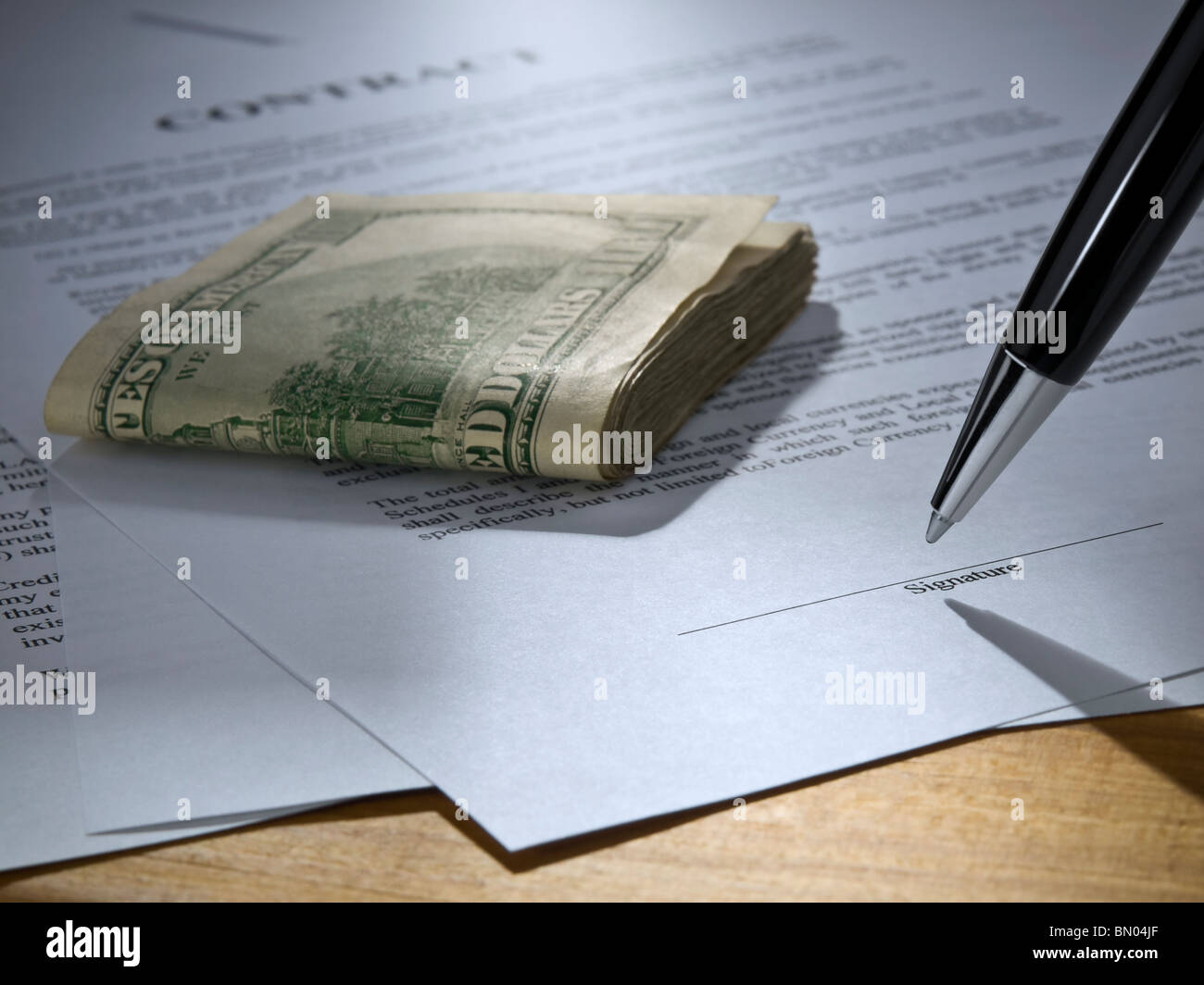 Close up of a pen about to sign the contract. Stack of money over it. Stock Photo