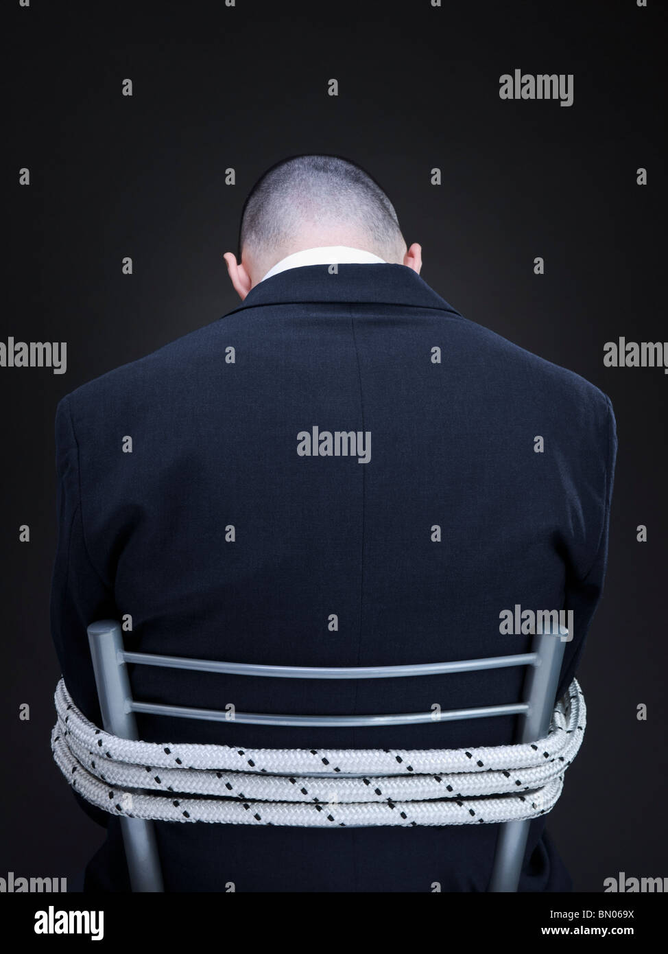 A businessman is tied up on a chair turning his back to the camera. Stock Photo