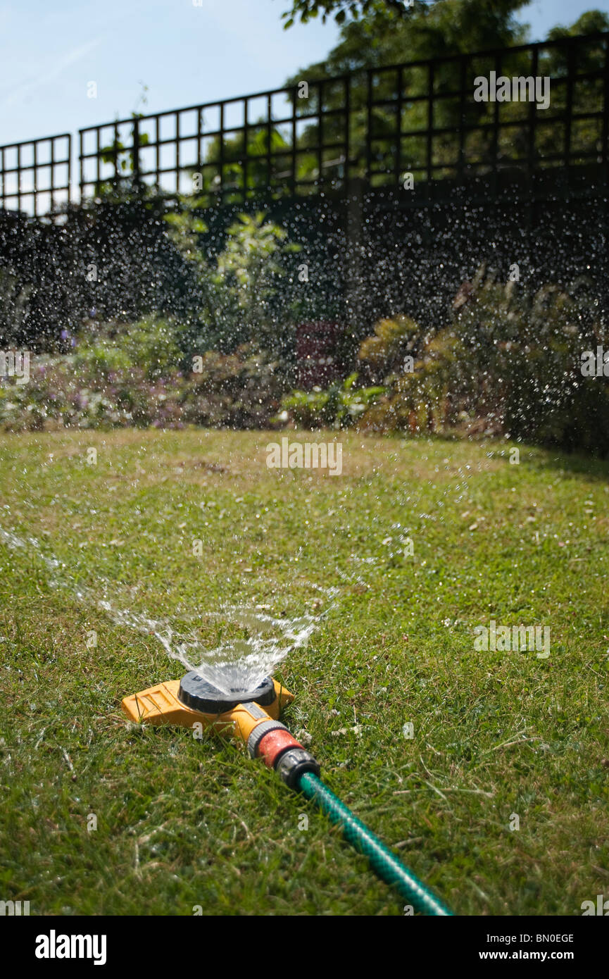 Water sprinkler irrigating a garden lawn Stock Photo
