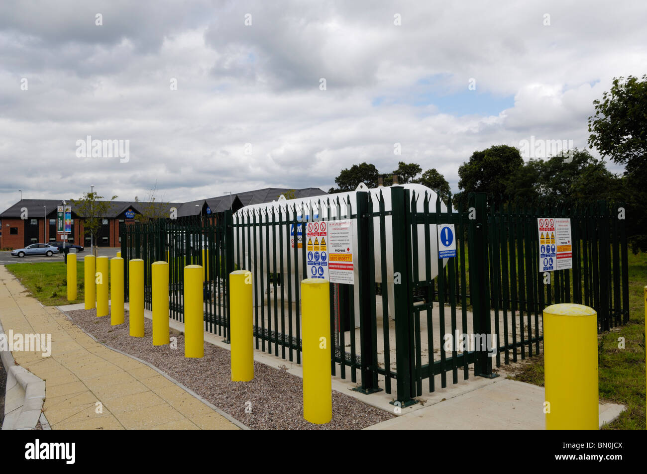 An LPG Propane tank at the back of a filling station surrounded by a safety fence and bollards. Stock Photo
