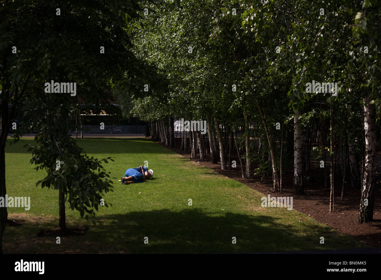 A construction worker still wearing his hard hat, takes a quick nap on the grass outside Tate Modern. Stock Photo