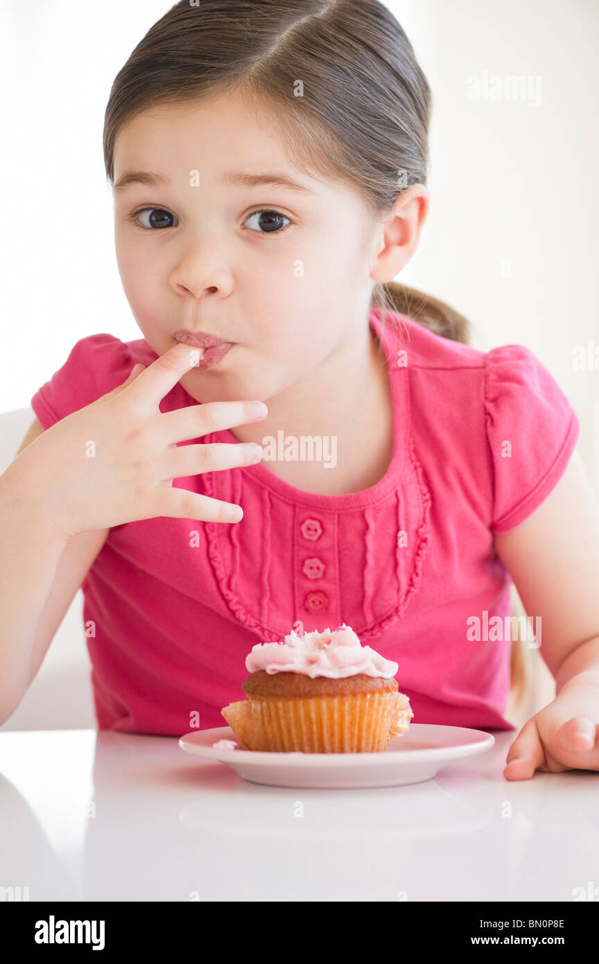Mixed race girl licking frosting from finger Stock Photo