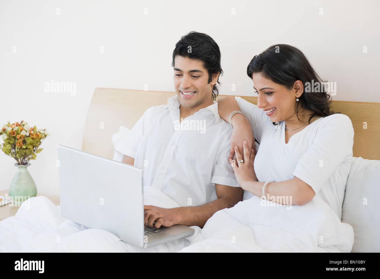 Couple using a laptop on the bed and smiling Stock Photo - Alamy