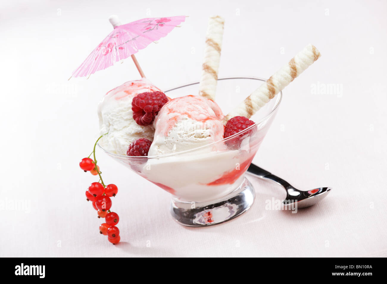Ice cream with raspberry, red currant, wafer sticks, and umbrella Stock Photo