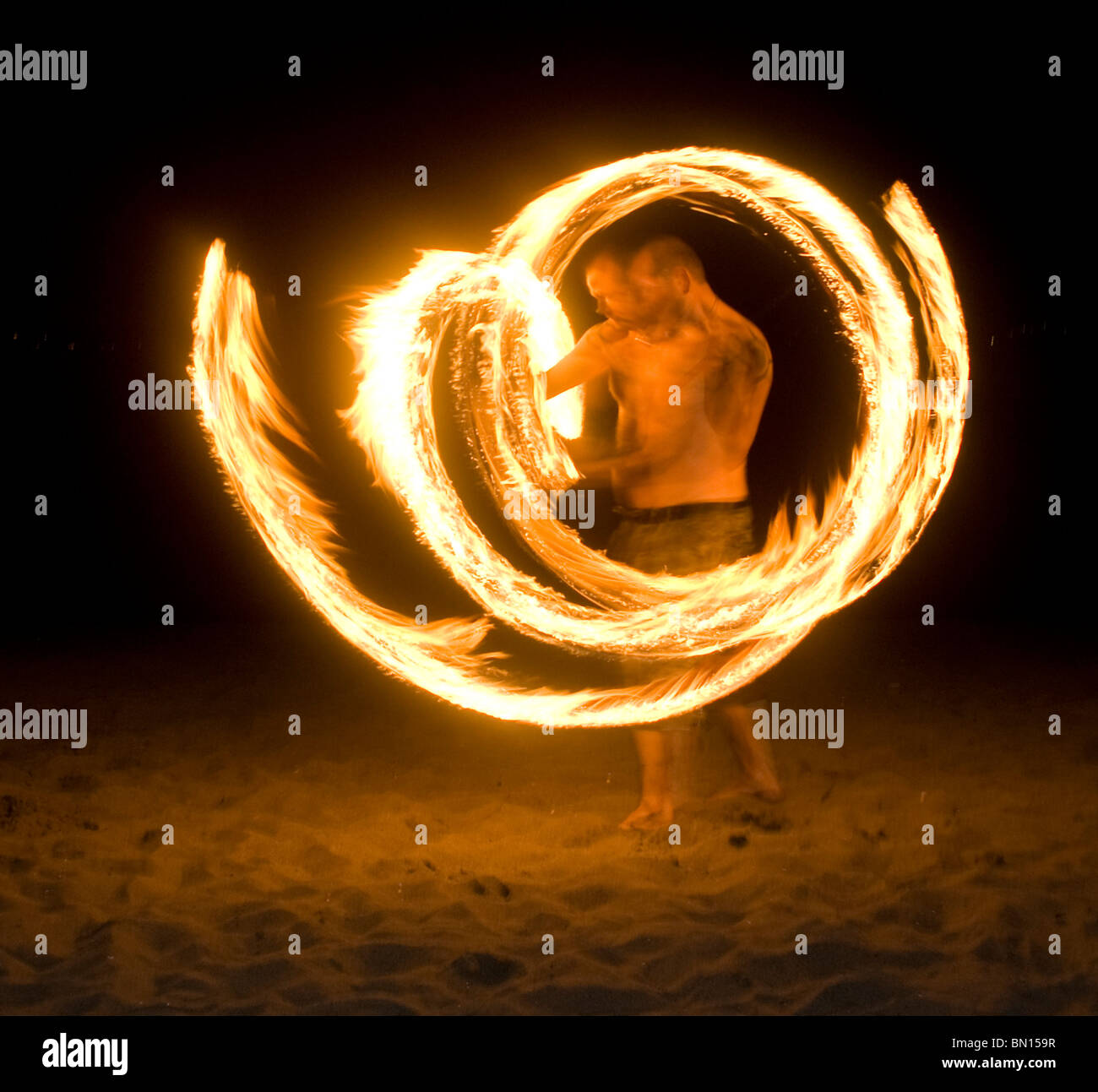 Person spins fire or fire dances at night on the beach Stock Photo