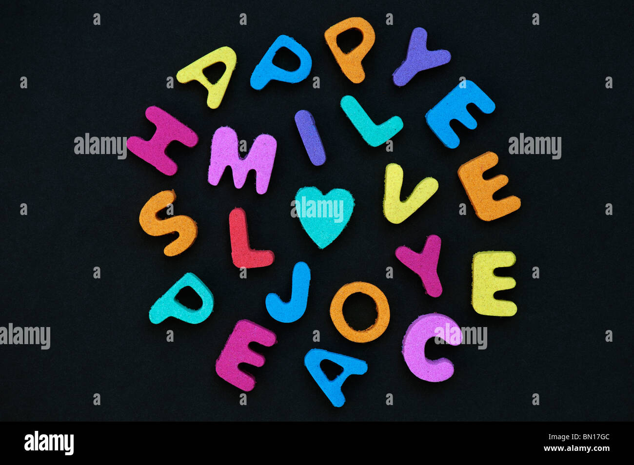 Multicoloured words LOVE SMILE HAPPY JOY and PEACE with a heart shape against black background Stock Photo