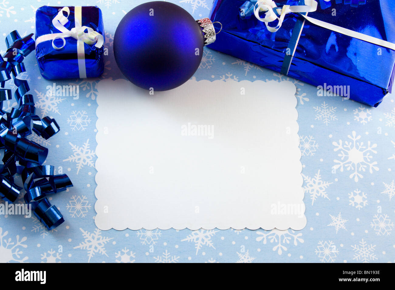 blank Christmas card with blue bauble, presents, curly ribbon on a snowflake background with copyspace Stock Photo